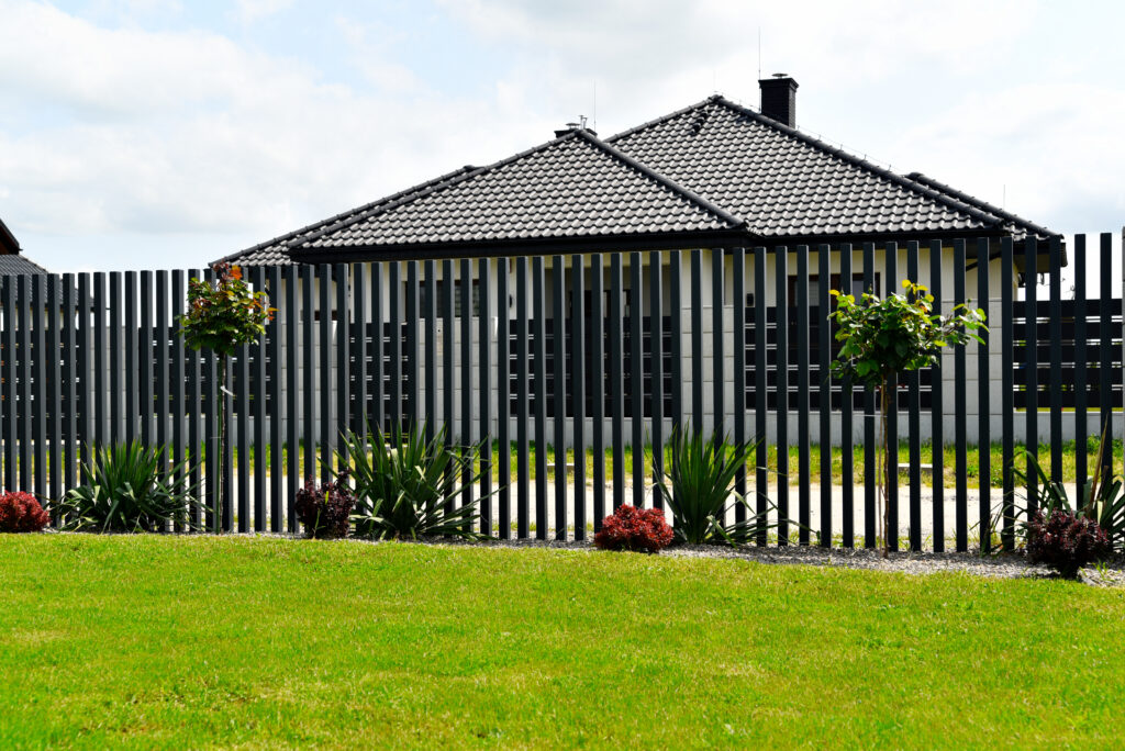 Nowoczesne ogrodzenie aluminiowe pionowe w stylu grzebieniowym na tle elewacji domu