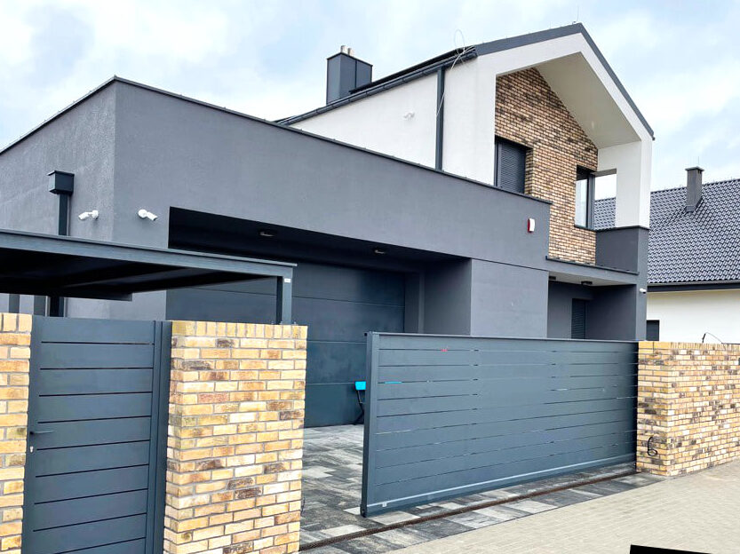 Na zdjęciu brama przesuwna, w tle nowoczesny dom. 