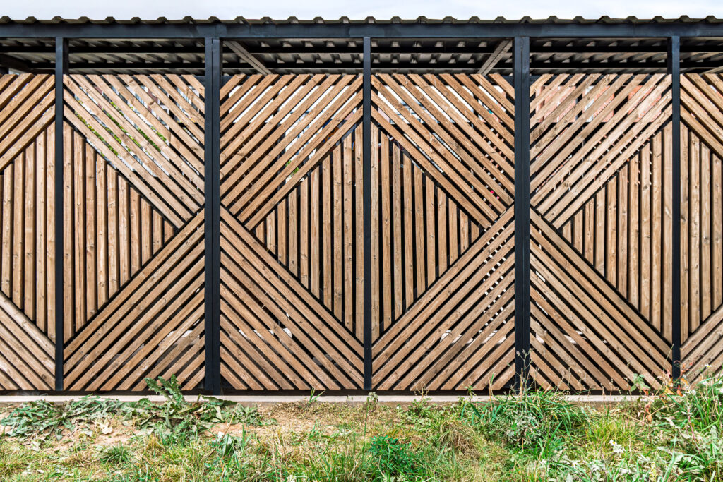 Interesujące geometrycznie ogrodzenie drewniane z zadaszeniem aluminiowym. 