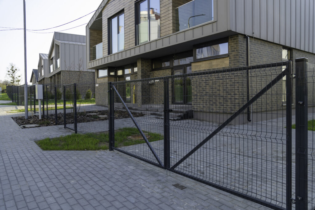 Przykład ogrodzenia panelowego - siatka na słupkach, w tle nowoczesne domy,